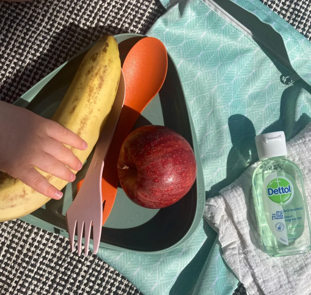 Taapero ottaa eväsrasiasta banaanin, rasiassa myös omena ja haarukka, rasian vieressä pul-pussi ja kestoliina sekä käsidesi